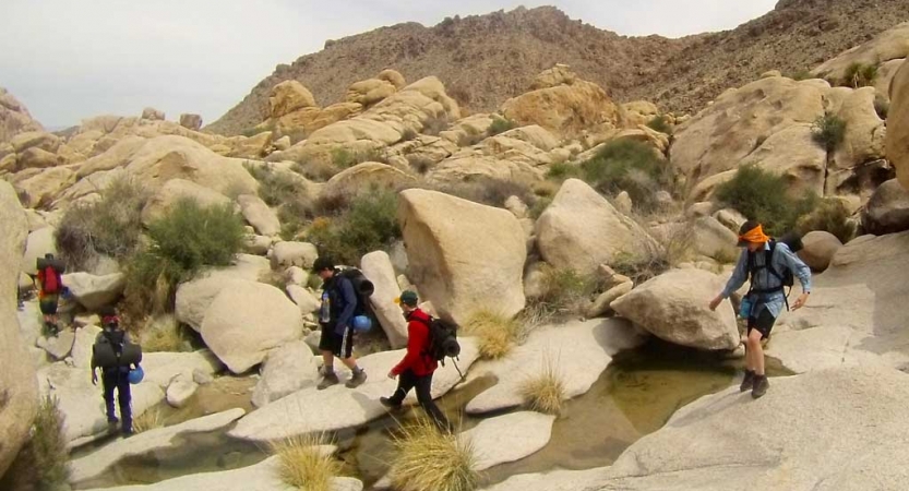 A group of people hike though large boulders. 